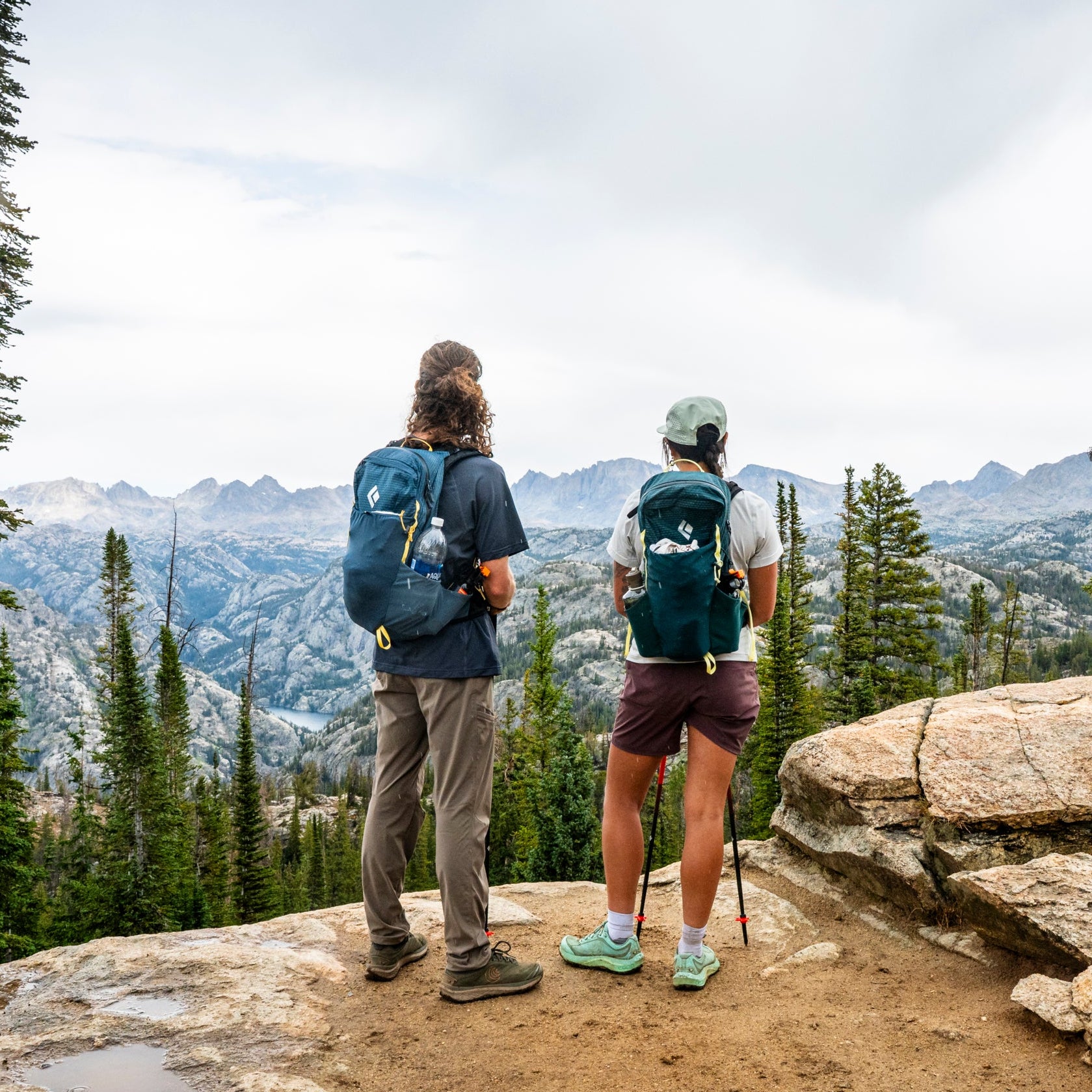 Two hikers wearing Black Diamond packs look out at a mountain vista. 