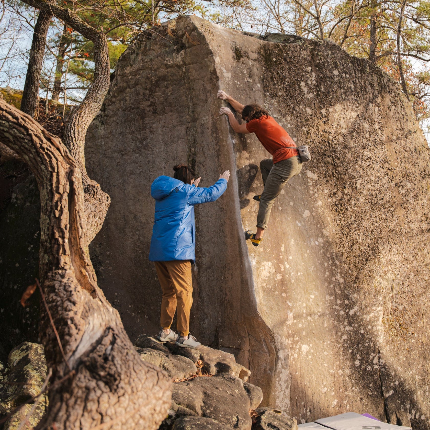 A bouldering works on the arete of a climb with a spotter. 